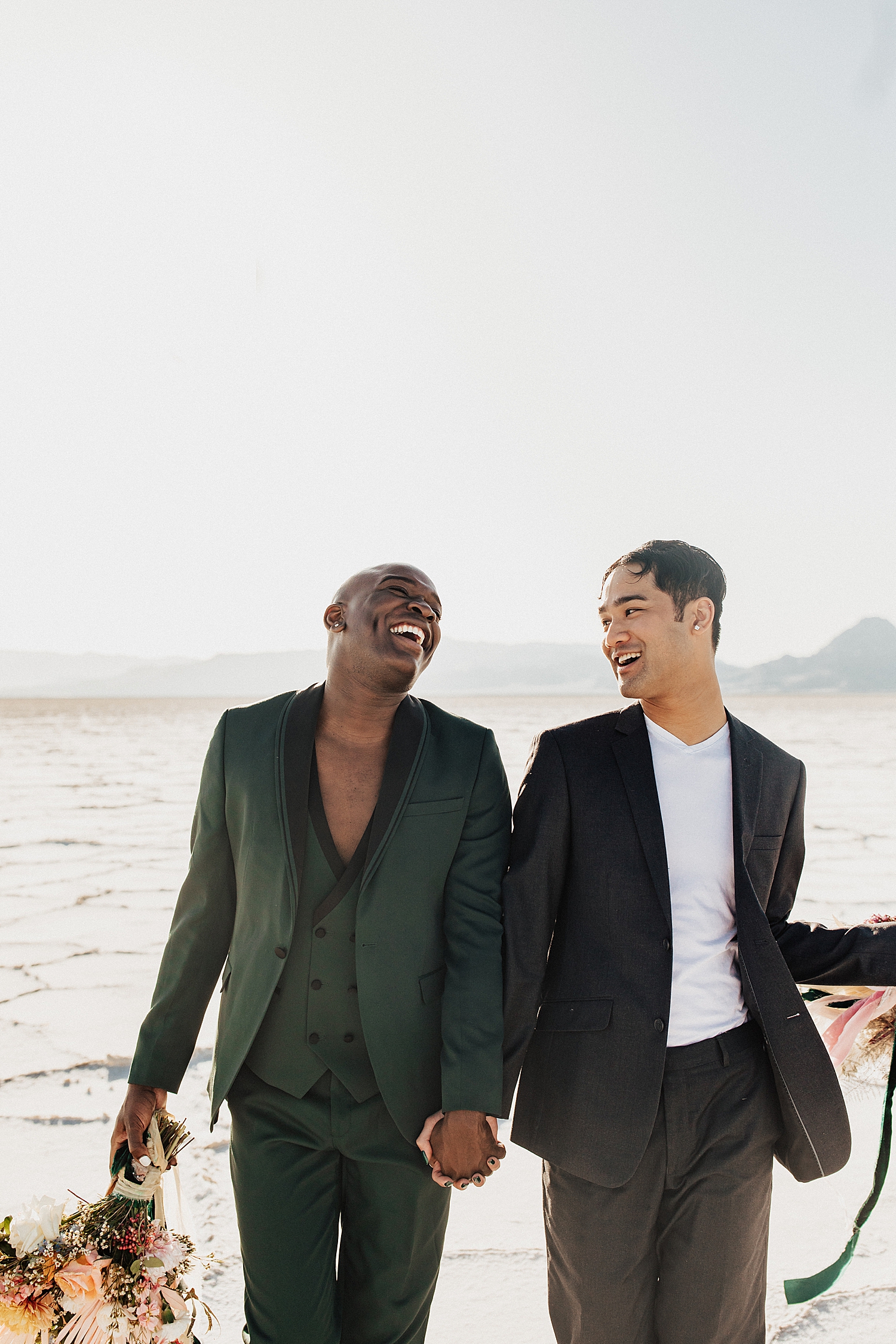 grooms walk hand in hand laughing together on the salt flats by Nicole Aston Photography