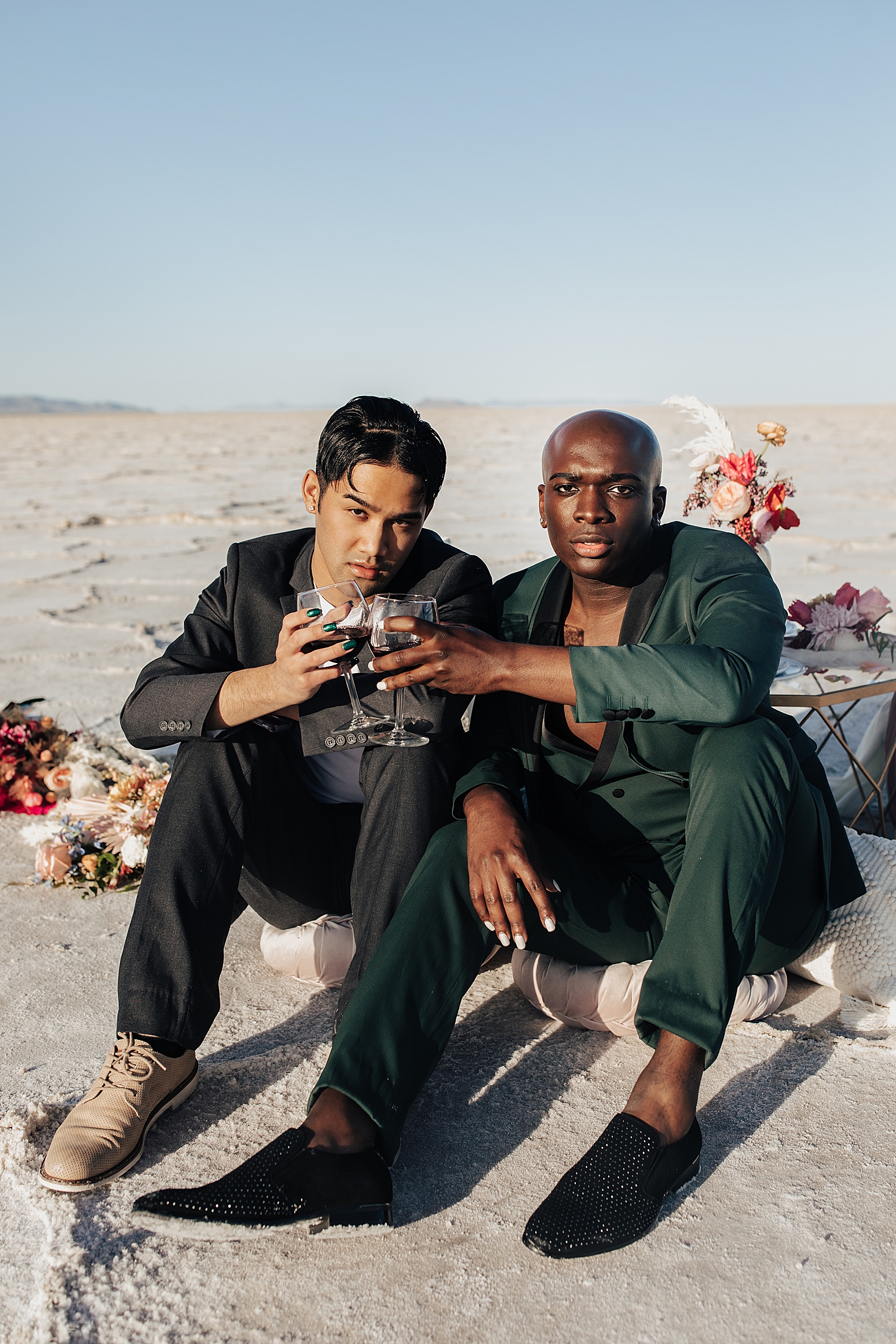 two men clink glasses while sitting in the salt flats by Destination wedding photographer