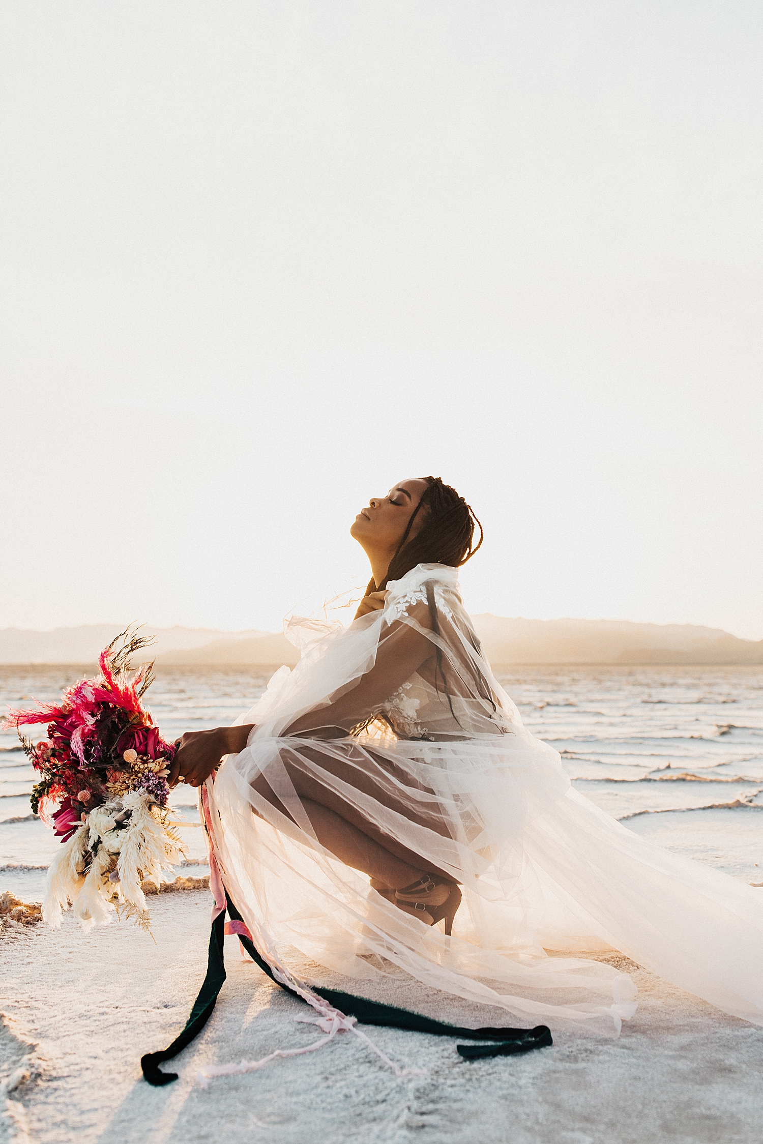 model kneels in lace & tulle gown in Utah desert by Nicole Aston Photography