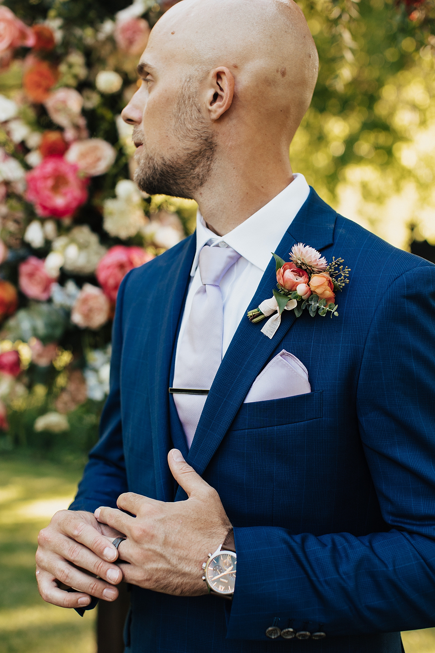 bald groom in navy suit with orange flowers pinned on at Log Haven Venue in Utah