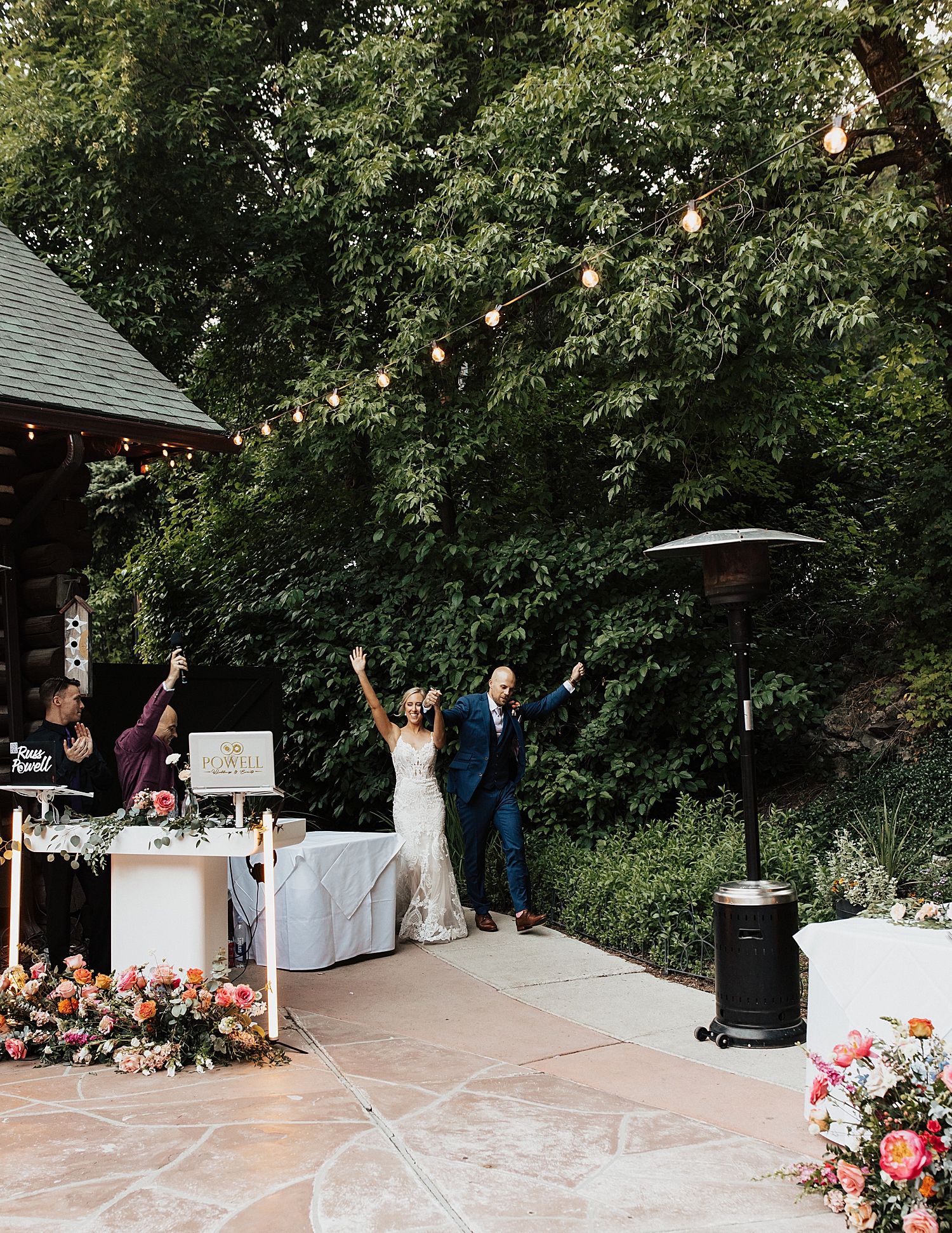 newlyweds enter outdoor reception with hands up at Log Haven Venue in Utah