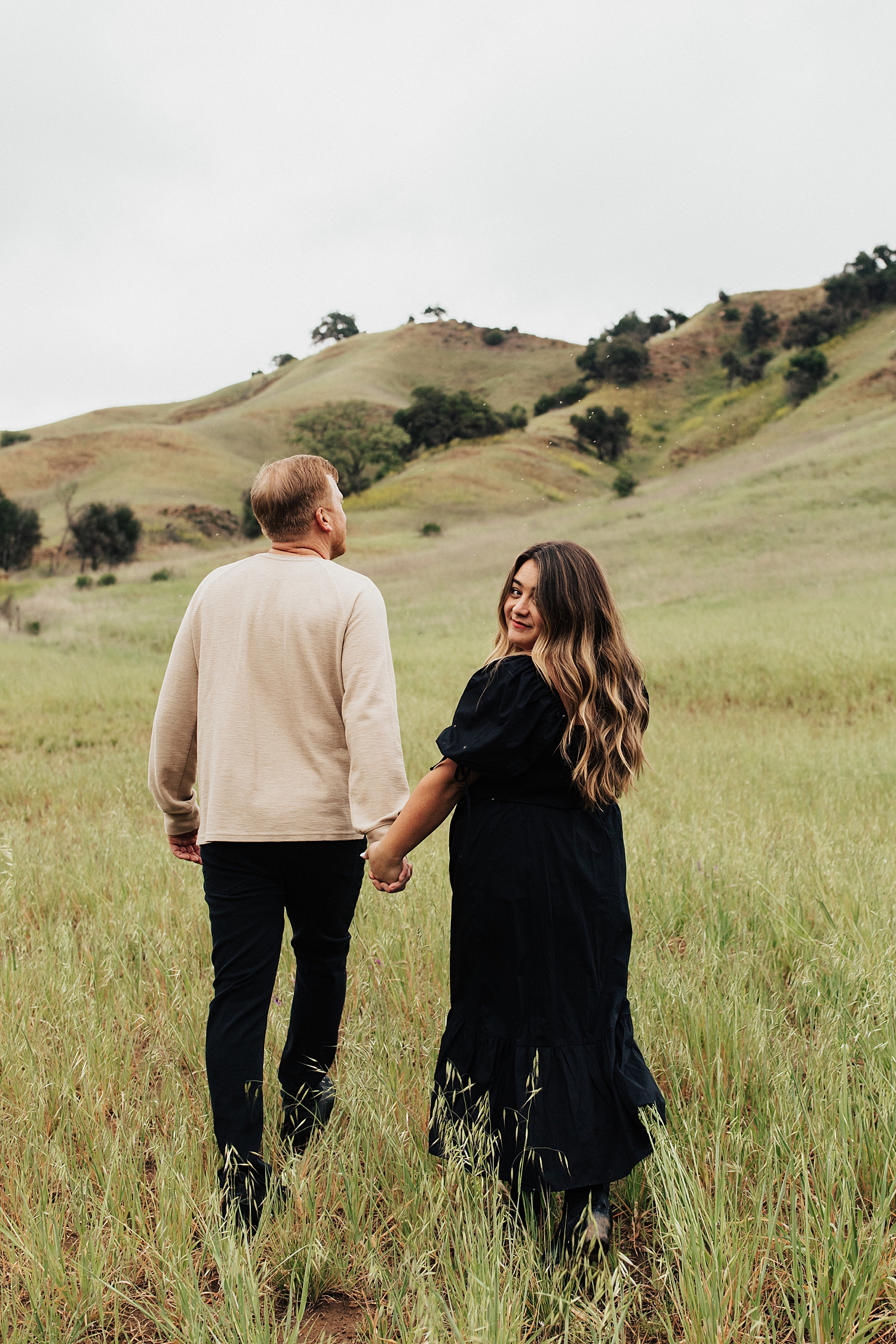 woman looks over her shoulder while walking through a field with man at Malibu Creek State Park