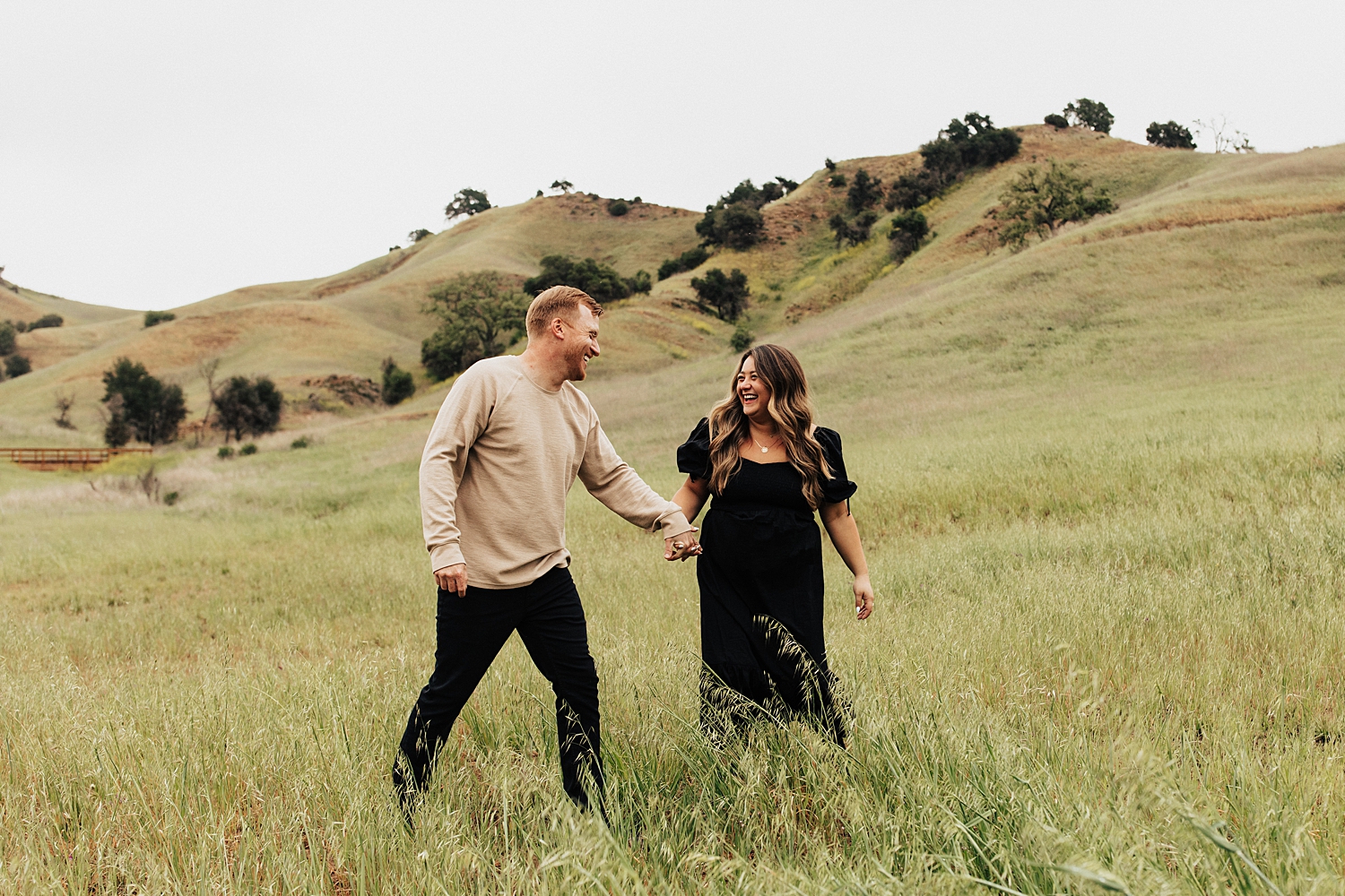 man and woman laugh while walking hand in hand in field by Destination wedding photographer