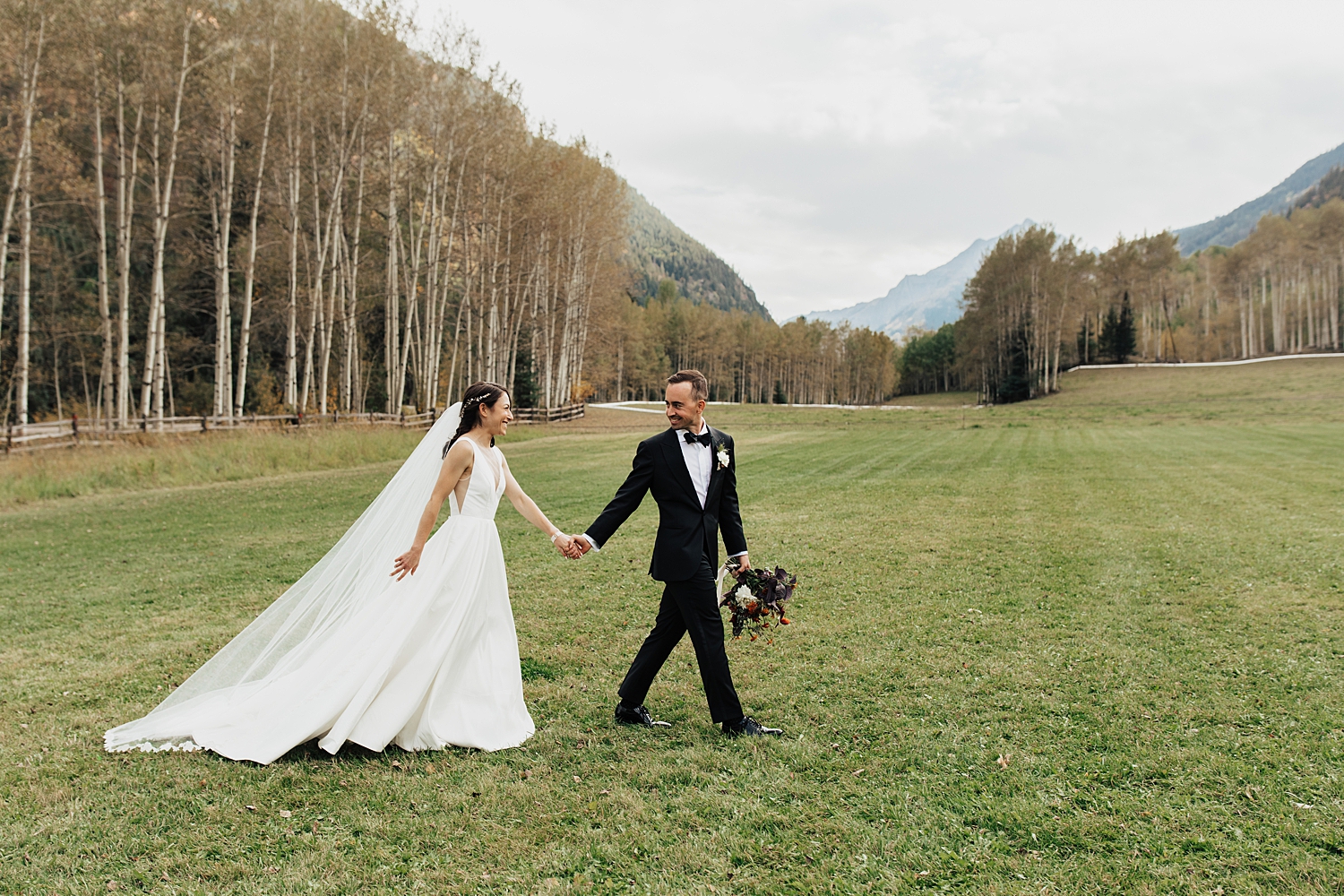bride and groom walk across big lawn for summer wedding in aspen