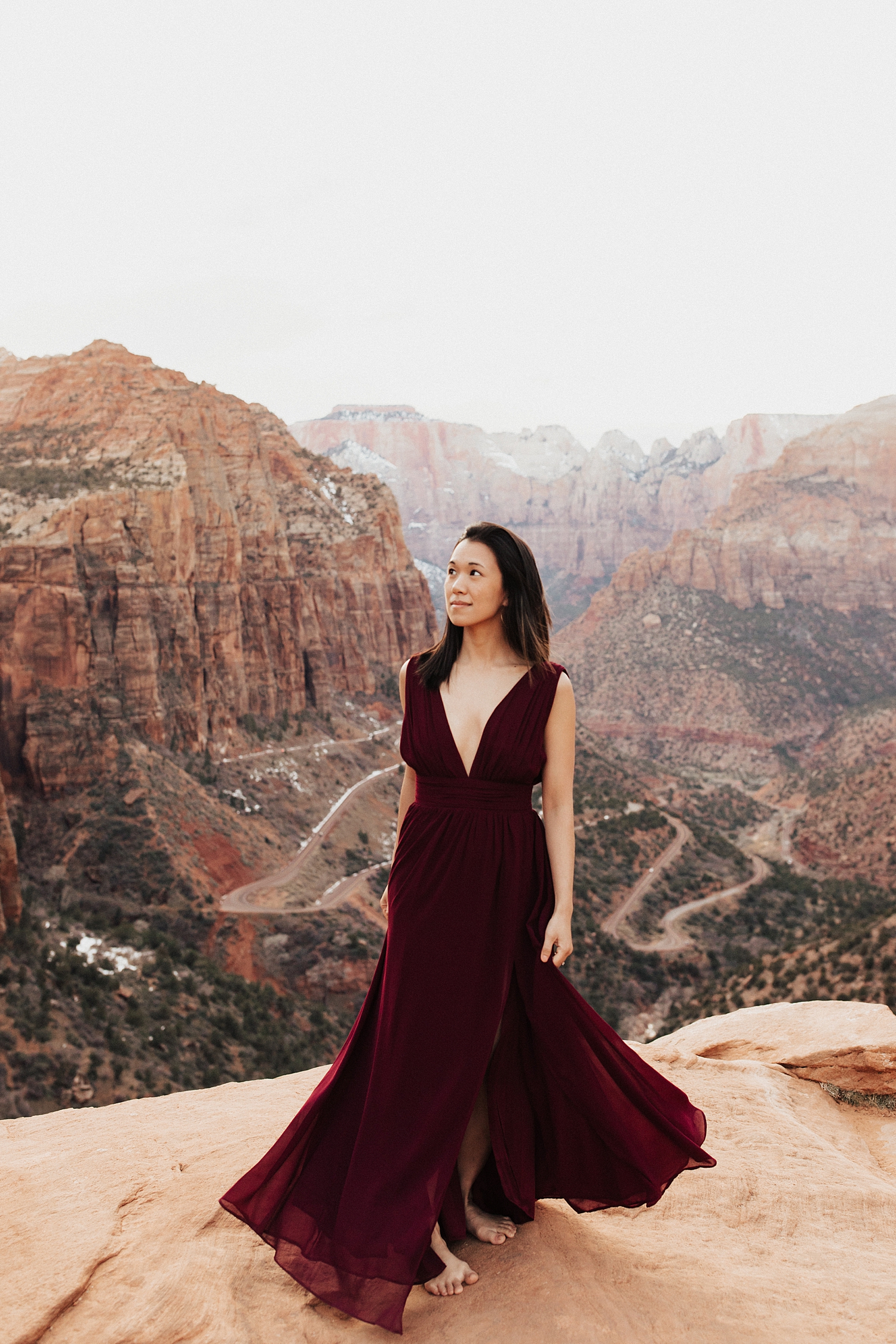 brunette in deep red dress walks on cliffside by Destination wedding photographer
