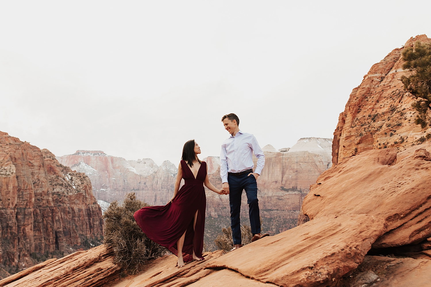 brunette in wine red dress stands with man on cliffside by Nicole Aston Photography