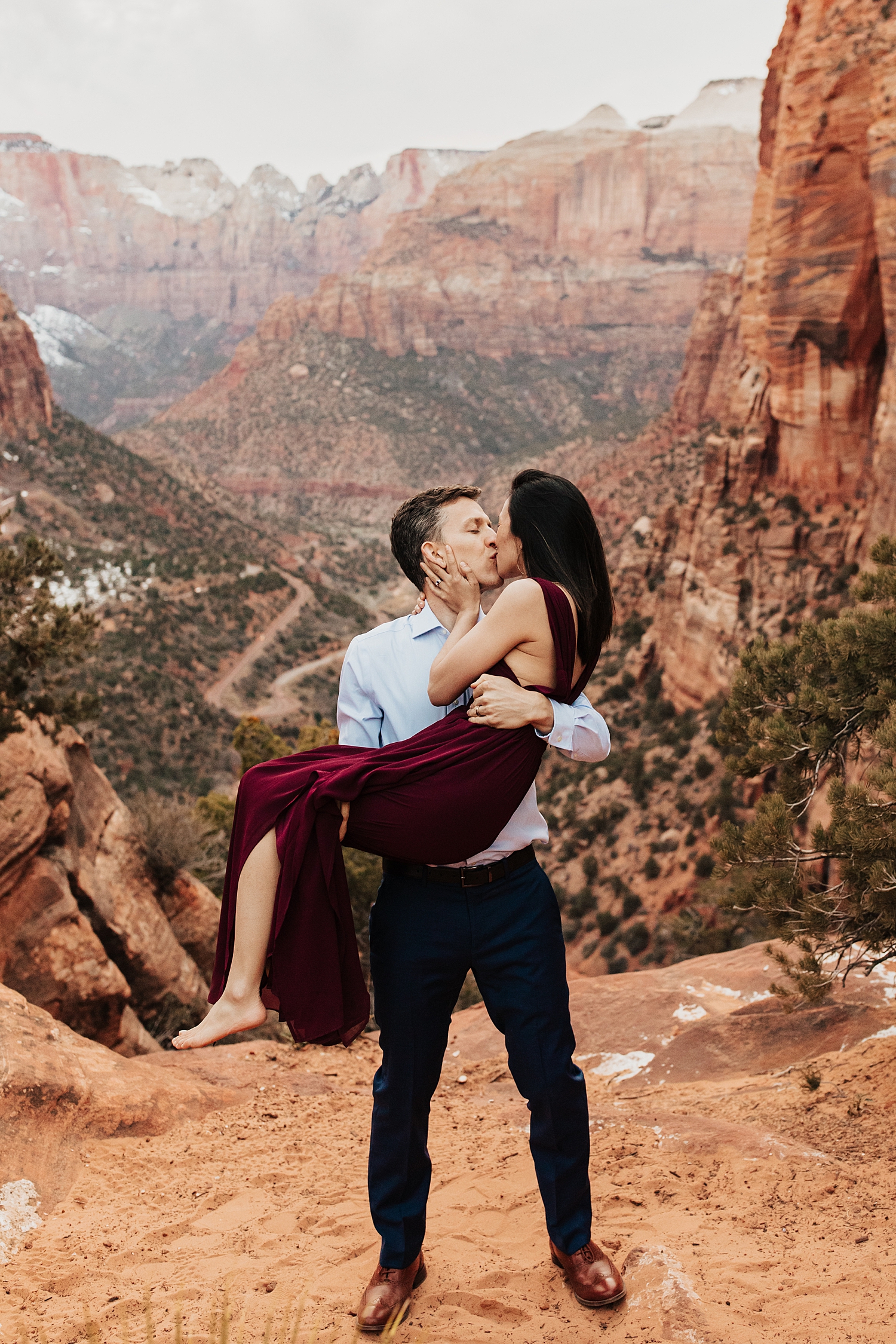 groom to be lifts up woman in red dress in rustic landscape by Destination wedding photographer