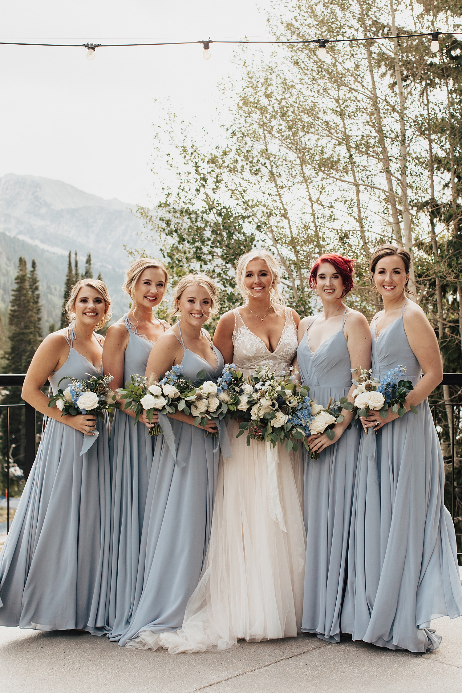 bride stands with bridesmaids wearing dusty blue gowns at Snowbird Mountain