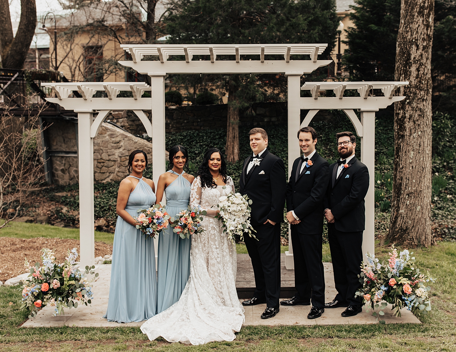 bridesmaids in blue and groomsmen in black surround couple by Destination wedding photographer