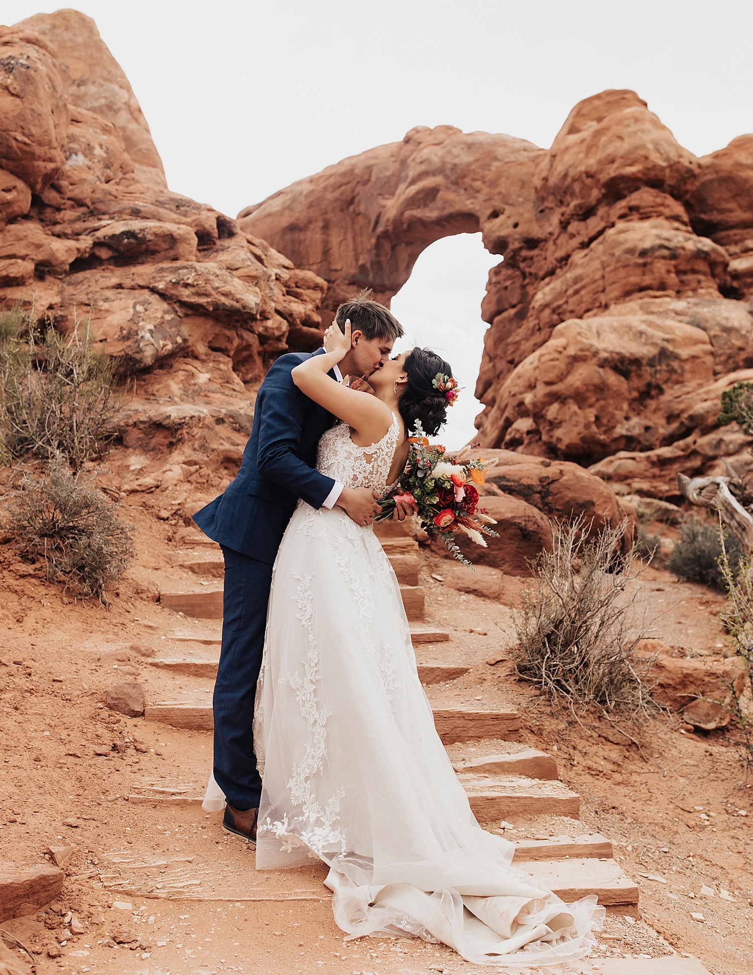 newlyweds share a kiss in front of red rocks arches by Nicole Aston Photography