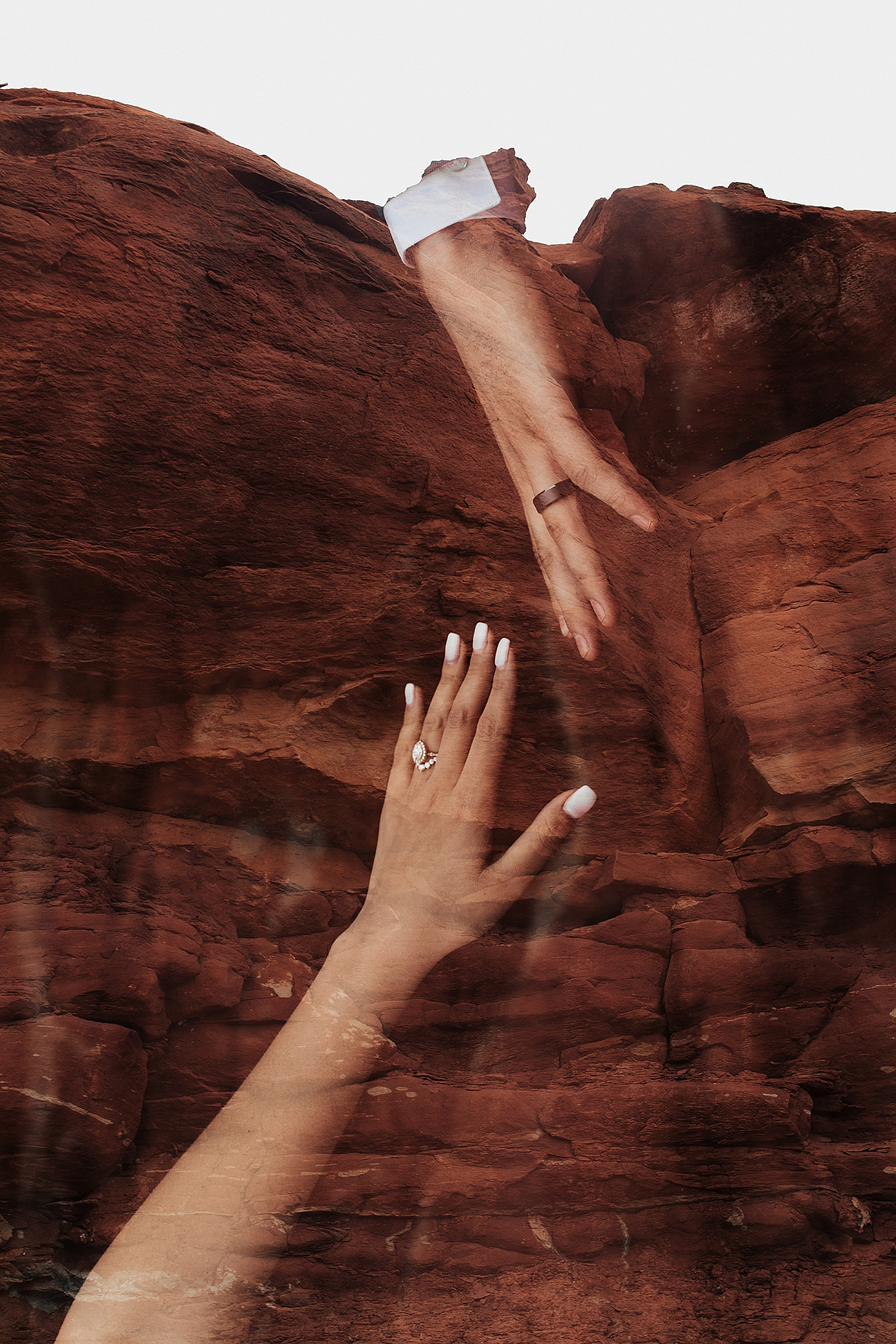 newly married couple reach hands across red rocks by Nicole Aston Photography