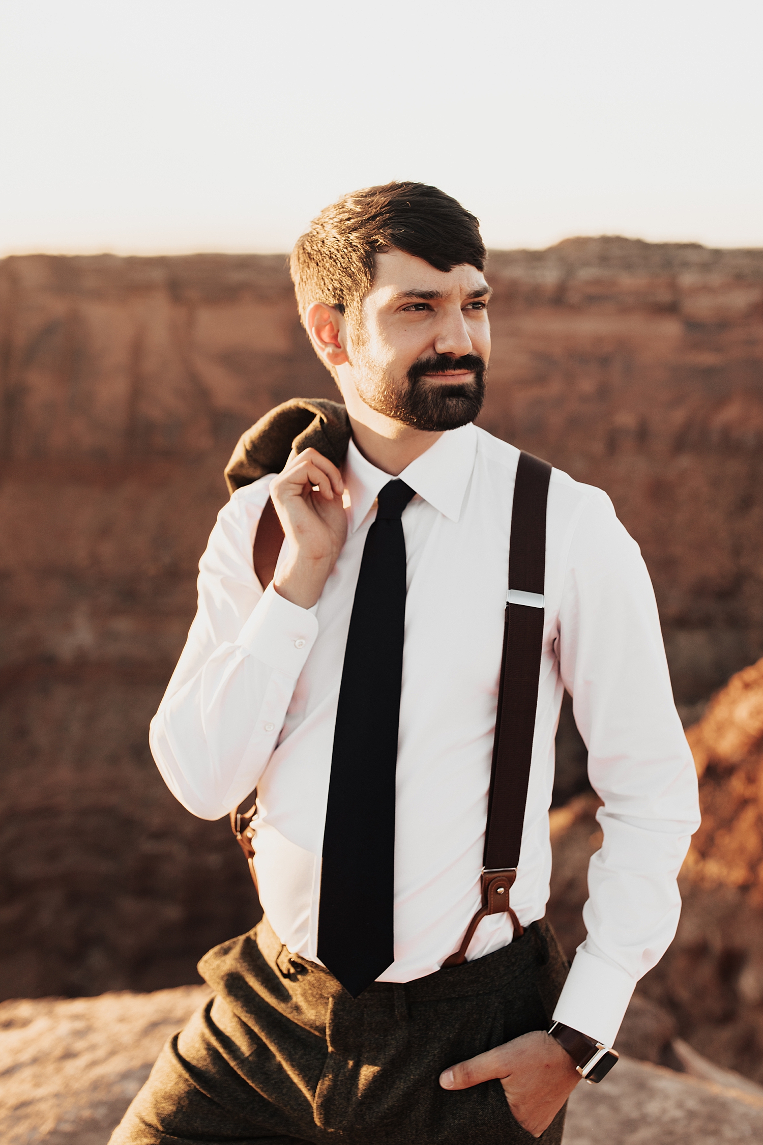 groom in suspenders stands with red rocks in the background by Destination wedding photographer