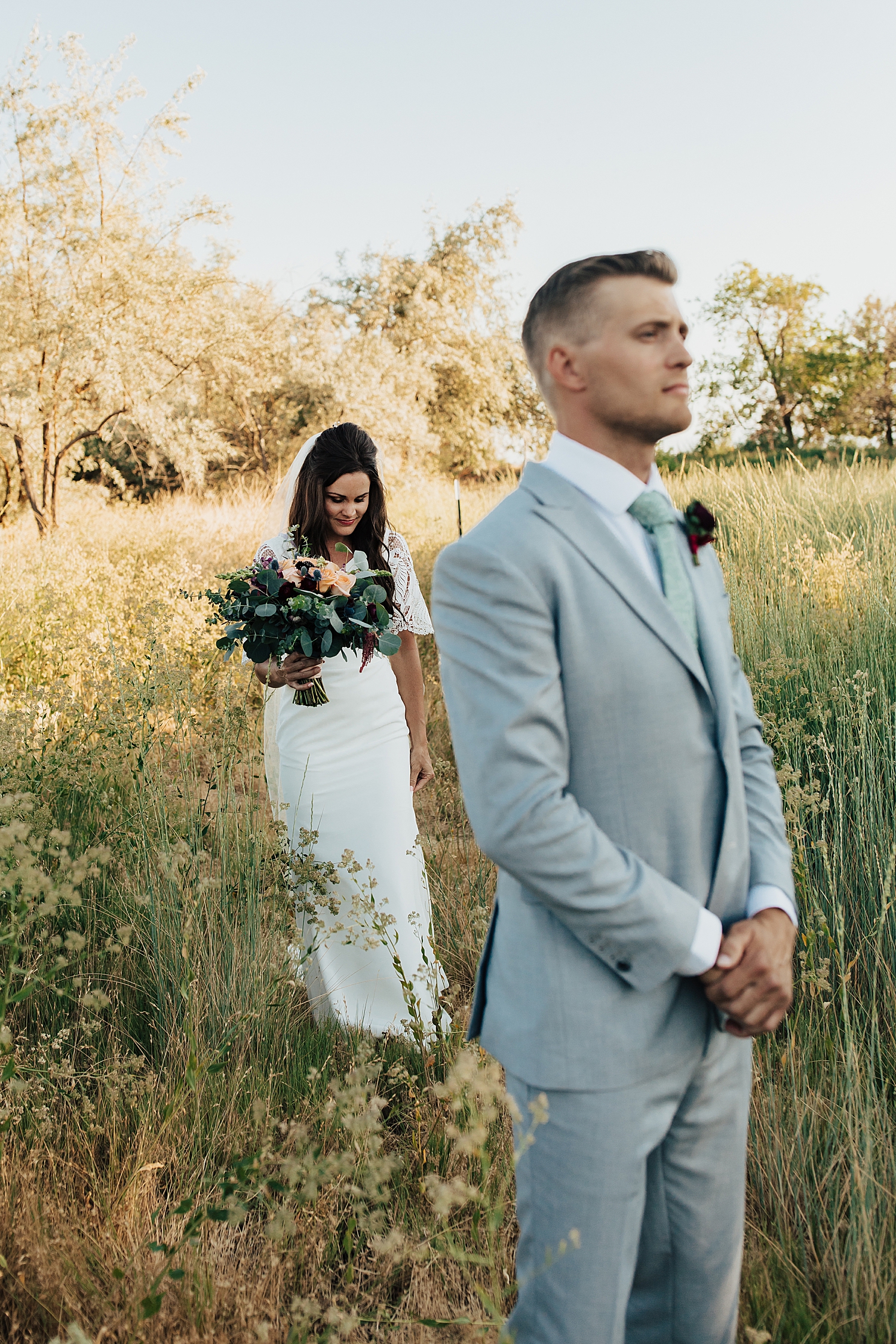 brunette woman in white dress approaches man for first look in field by destination wedding photographer
