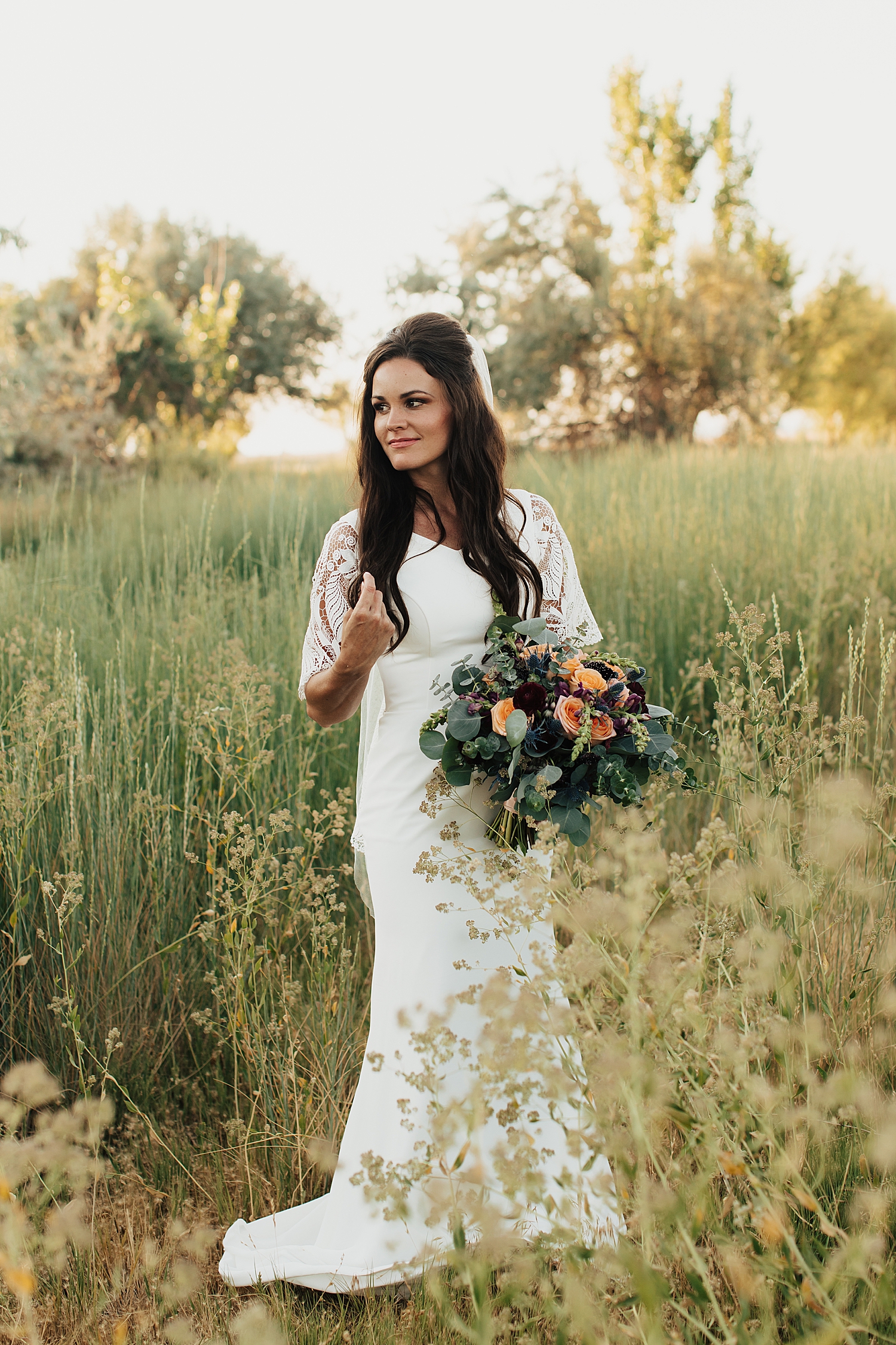 brunette bride carries flowers through a big field by Nicole Aston Photography