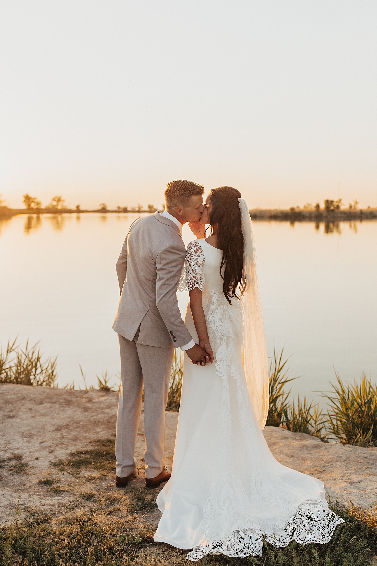 brunette bride leans in to kiss husband during sunset at bountiful pond