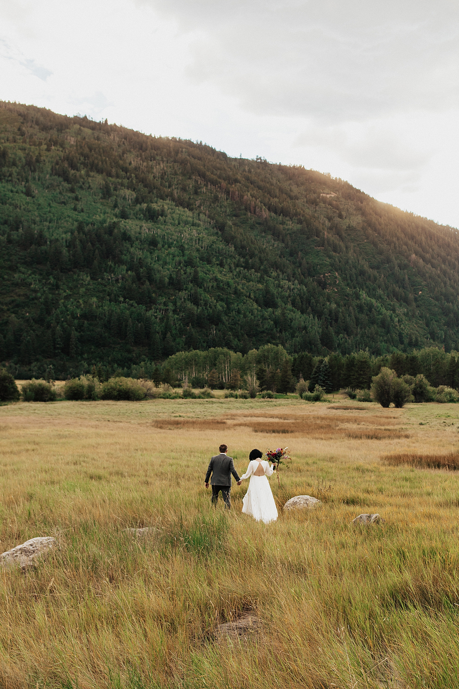 couple wanders through mountain field during golden hour by destination wedding photographer
