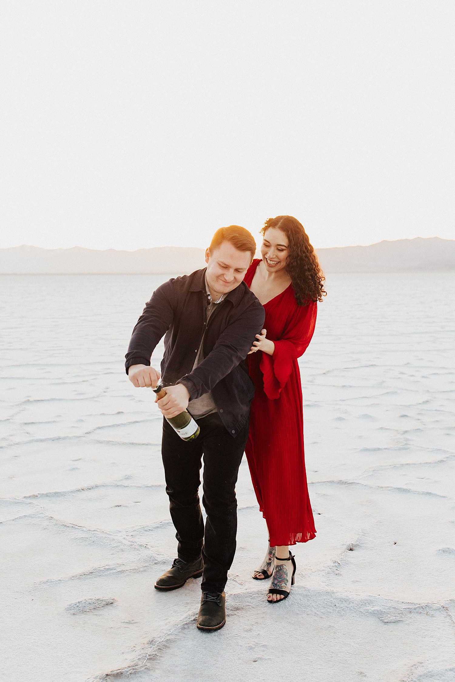 brunette couple pop a bottle of champagne in desesrt landscape by Destination wedding photographer