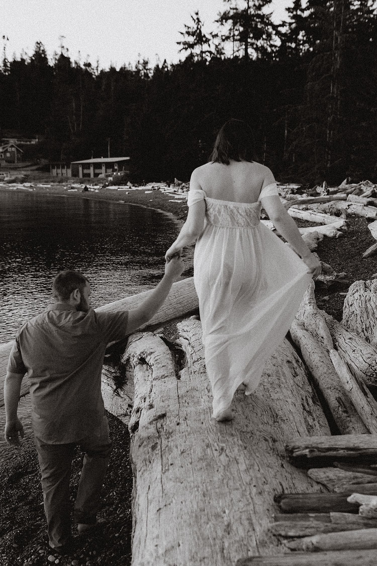 woman in dress walks on log holding man's hand at Rosario Beach