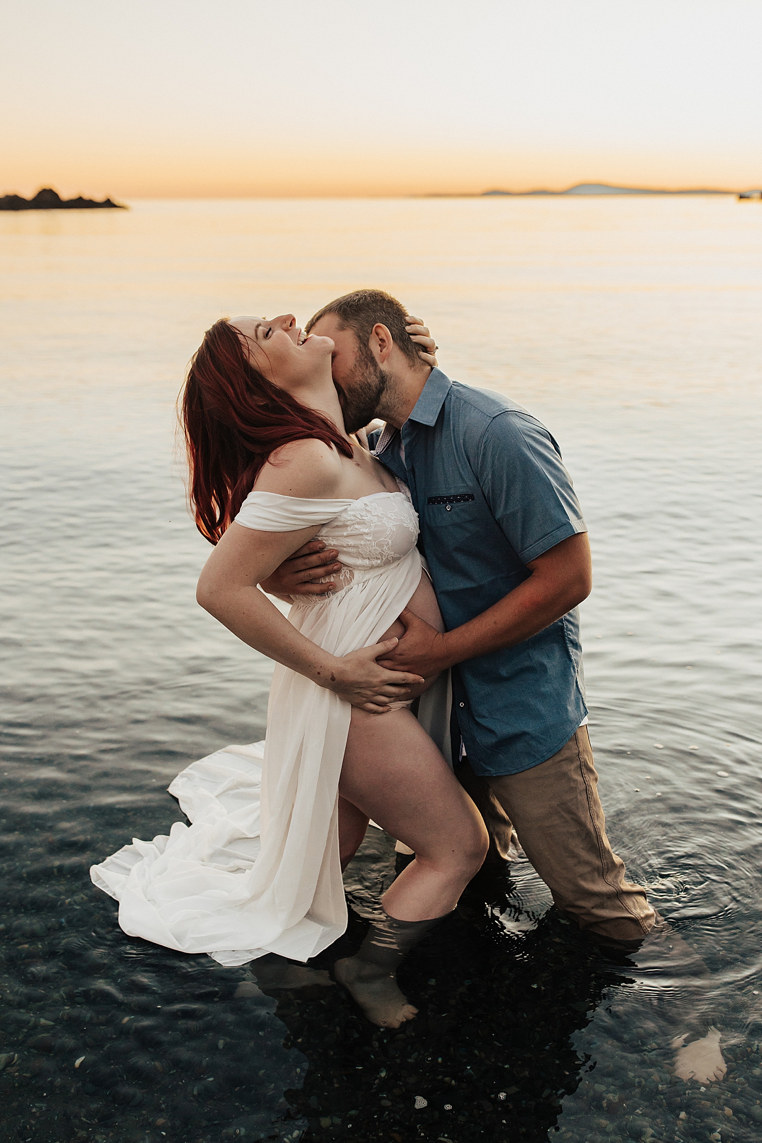 husband kisses wife neck in the ocean while cradling her baby bump by Nicole Aston Photography